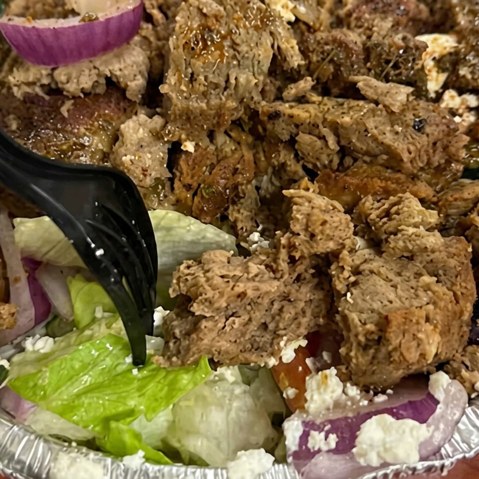 Loaded salad bowl with lettuce, tomatoes, red onion, feta cheese, olives, and crispy fried meat pieces, served with a black fork.