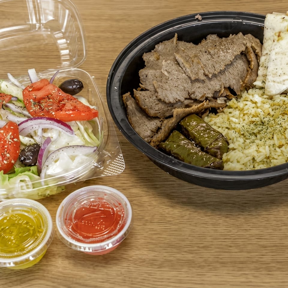 Greek-style meal with gyro meat, rice, stuffed grape leaves, pita, salad, and dipping sauces on a wooden table.