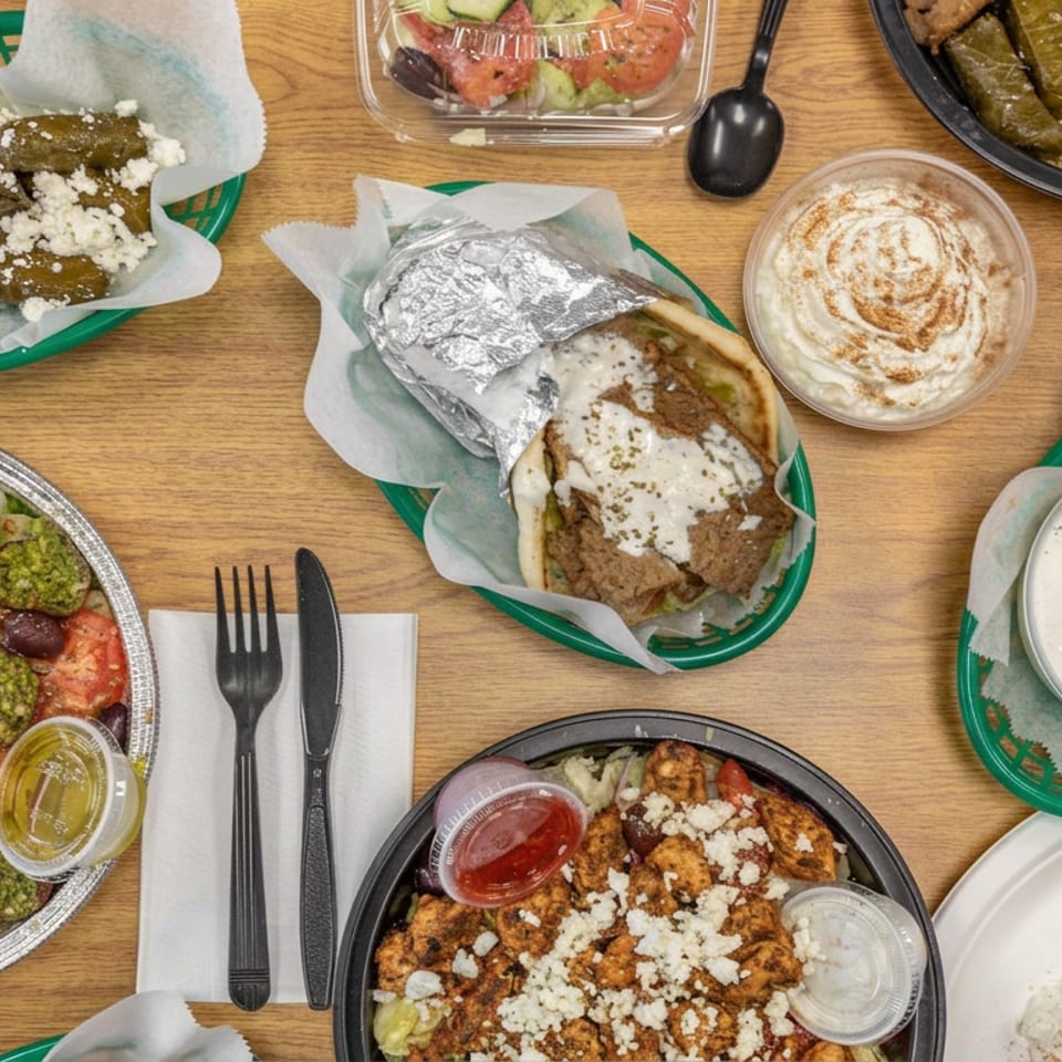 Overhead view of a Mediterranean meal featuring pita, falafel, shawarma, salad, stuffed grape leaves, dips, and rice on wooden table.