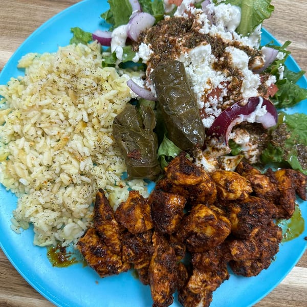 A Greek plate with chicken, rice, salad, feta, red onions, and stuffed grape leaves.