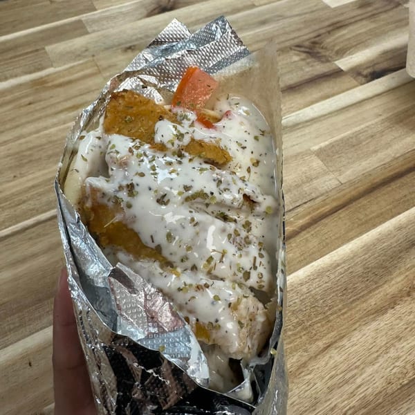 A Mister Mike's Gyros chicken pita, generously topped with tzatziki sauce and herbs, wrapped in foil.