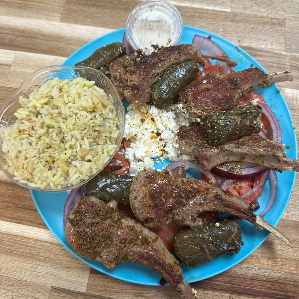 Mister Mike's Gyros lamb chops with dolmades, rice, feta, tomatoes, and onions on a blue plate.